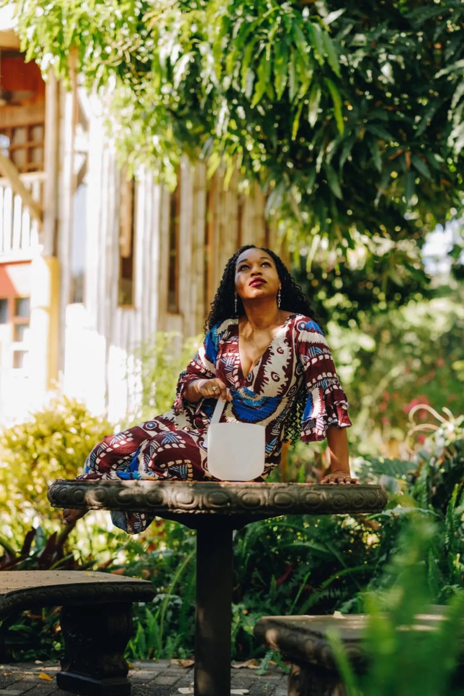 Stephanie Ann Ball seated in a garden, playing a crystal singing bowl